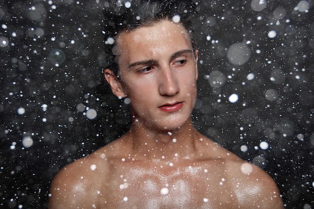 雪、冬、クリスマス、人々、スキンケア、美容のコンセプト-黒い雪の背景に黒い髪の濡れた若い男。剃った胸を持つ肖像画の男性。男性のスキンケア。 Premium写真