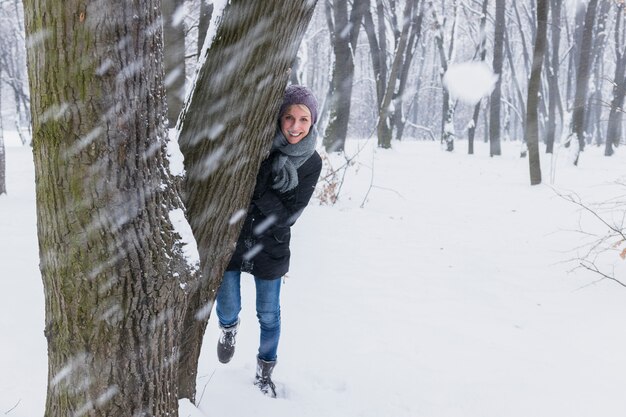 Snowball in front of smiling woman standing behind the tree