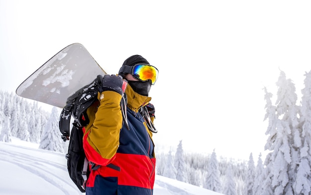 Snowboarder in protective glasses holding his snowboard on his back