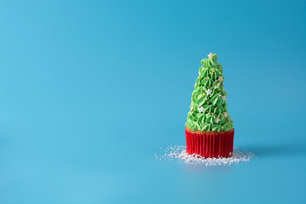 青い背景に分離されたクリスマスツリーのカップケーキに雪が降る
