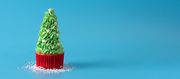 青い背景に分離されたクリスマスツリーのカップケーキに雪が降る