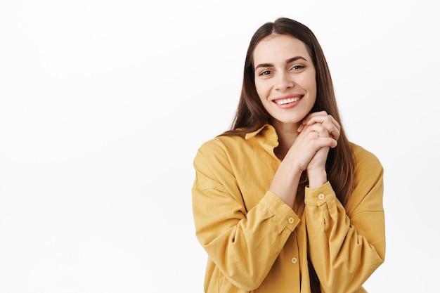 So cute, thank you. Smiling lovely woman being touched by gift, holding hands together and looking thankful, gazing at something beautiful with admiration and joy, white background