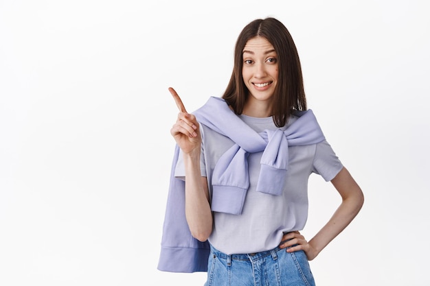 Not so fast, look up. Sassy young woman shaking finger and pointing at upper left corner, showing logo banner, advertisement, standing against white background