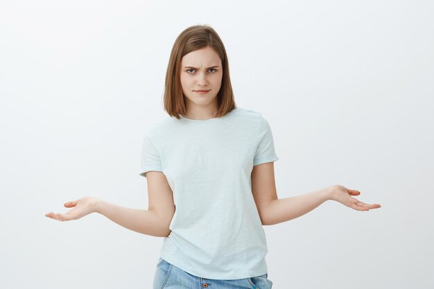 So what. Portrait of serious-looking irritated and confused good-looking female looking from under forehead pursing lips and looking annoyed with hands spread aside in questioned displeased gesture