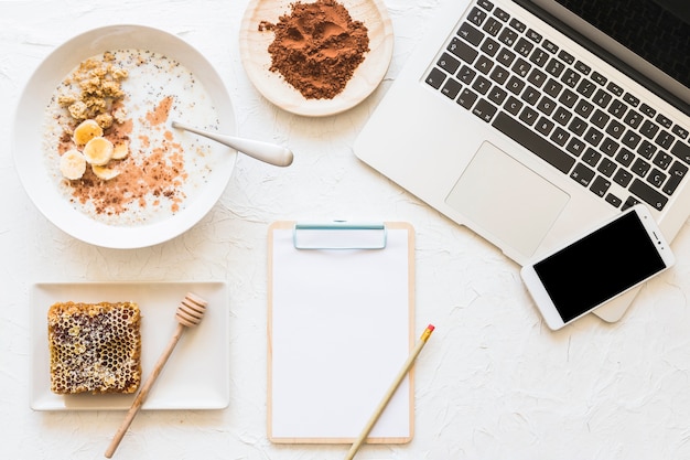 Foto gratuita farina d'avena inzuppata e nido d'ape con laptop e cellulare sul posto di lavoro