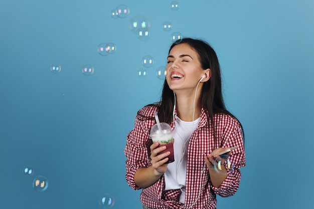 Palloncini di sapone volano intorno a una ragazza felice che beve latte e balla con gli auricolari