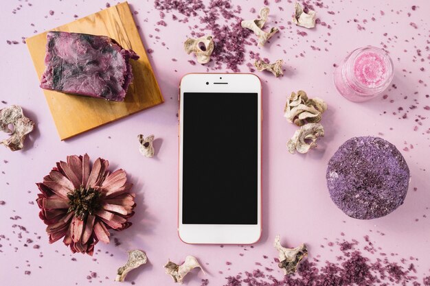 Soap bar; herbal body scrub; dried flower and smartphone on pink background