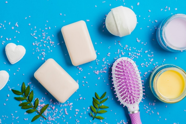 Soap; bath bomb; moisturizer cream and hairbrush on blue background