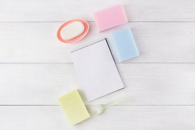 Free photo soap; different type of sponge; spiral notebook and plastic brush on wooden background