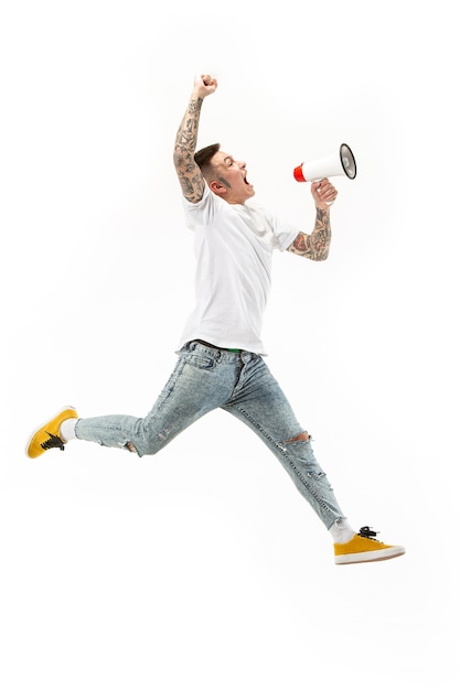 Soccer fan jumping on white background. young man as football fan with megaphone isolated on orange studio. Support concept.