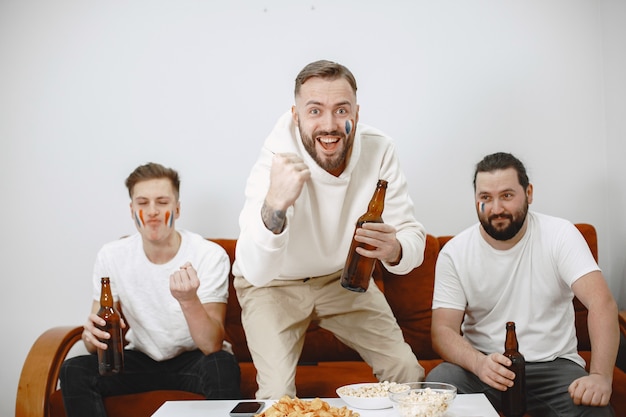 Бесплатное фото Футбольные фанаты сидят на диване в гостиной и пьют пиво