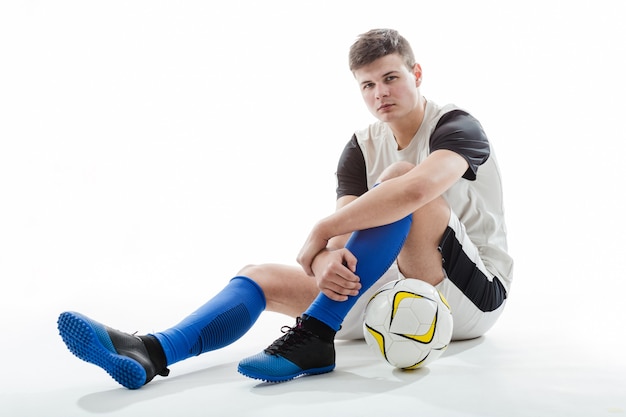 Foto gratuita calciatore con la sfera che si siede sul pavimento