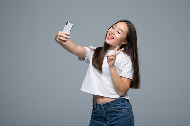 Sociable beautiful asian girl taking selfie or speaking on video call using cell phone over gray background