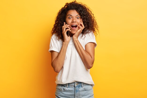 Sociable friendly young woman with curly hair posing with her phone