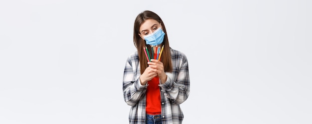 Free photo social distancing leisure and hobbies on covid19 outbreak coronavirus concept thoughtful cute dreamy woman in medical mask decide which colored pencil choose pondering what draw