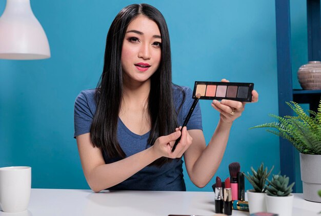 Social media influencer holding make up palette showing at camera while doing beauty tutorial advertising cosmetic product. Asian content creator recording cosmetic review for vlogging channel