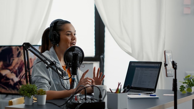 Free photo social media star putting on headphones while starting video blog and talking to audience. joyful internet content creator filming daily vlog with smartphone while speaking to public about her day.