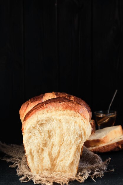 Soft brioche broken in half on wooden board Honey in glass bowl in the background Traditional sweet French brioche baked concept Closeup selective focus the buns on burlap bed vertical frame
