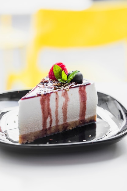 Soft cake topped with raspberry; mint; blueberry & chocolate sauce served on black plate against blur backdrop