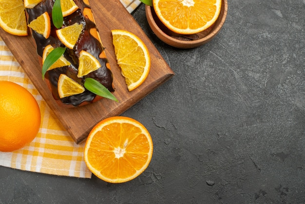 Soft cakes whole and cut oranges with leaves on dark table