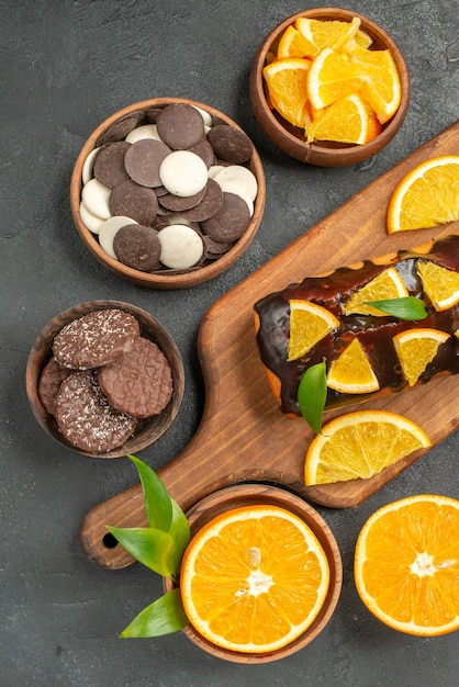 Soft cakes on wooden cutting board and cut oranges with leaves biscuits on dark table