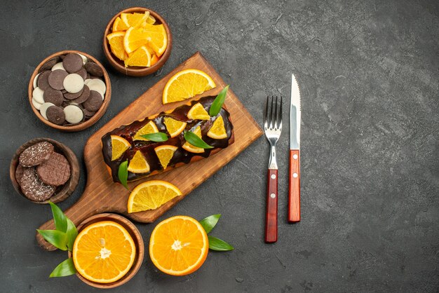 Soft cakes on wooden cutting board and cut oranges with leaves biscuits on dark table