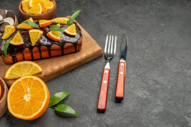 木製のまな板に柔らかいケーキと葉ビスケットフォークとナイフでオレンジをカット