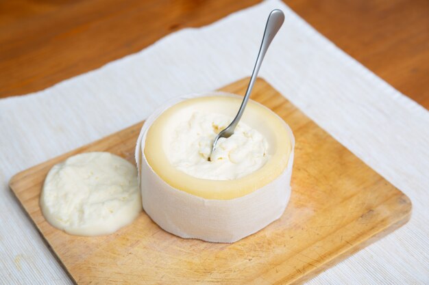 Soft cheese with cut top standing on wooden board