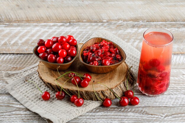 Soft drink with cherries, wooden board, jam in a jug on wooden and kitchen towel high.