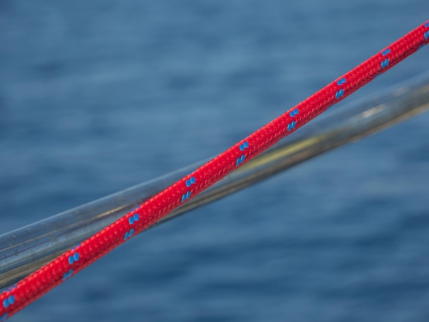 Мягкий фокус красной лодочной веревки, натянутой на лодке на фоне синих вод