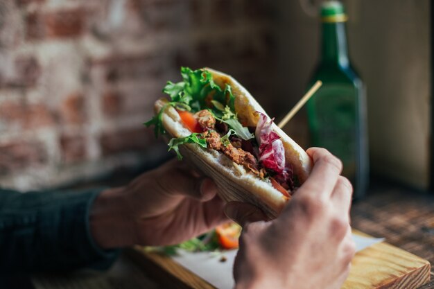 Soft focus shot of man having delicious huge breakfast at cool restaurant or cafe, puts guacamole or avocado spread on top of rye bread toast