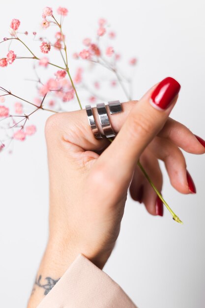 Soft gentle photo of woman hand with big ring red manicure hold cute little pink dried flowers on white.