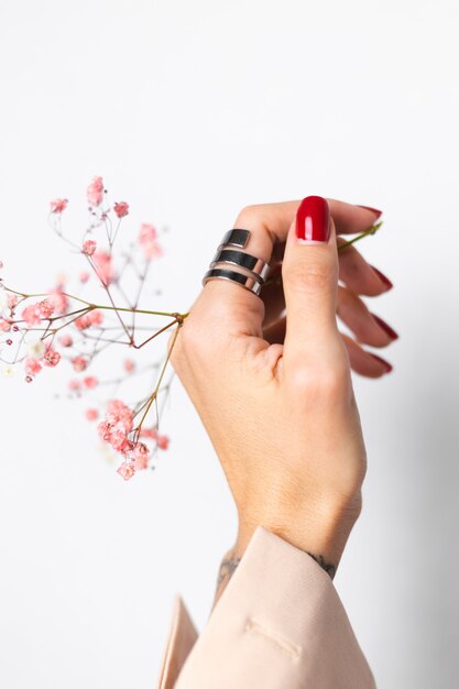 Soft gentle photo of woman hand with big ring red manicure hold cute little pink dried flowers on white.