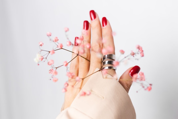 Soft gentle photo of woman hand with big ring red manicure hold cute little pink dried flowers on white.