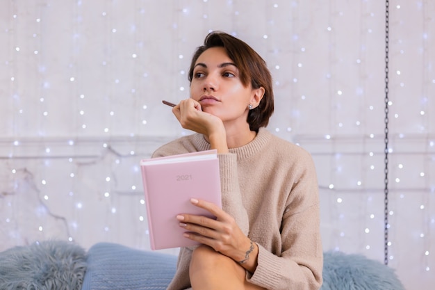Мягкое фото женщины в удобном свитере и шерстяных носках дома, сидящей на кровати зимой с табличкой для ноутбука 2021