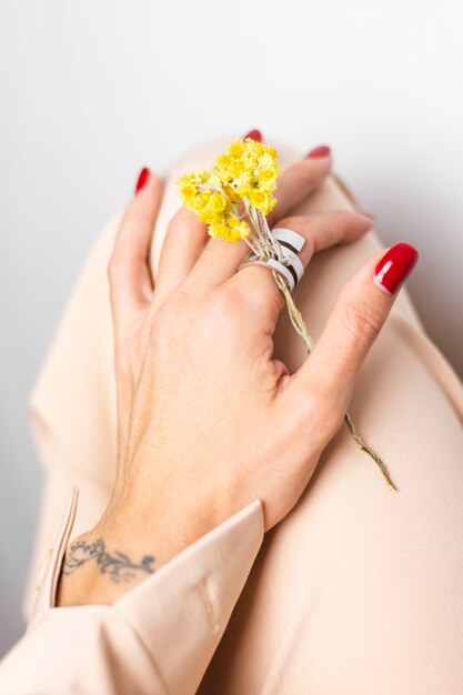 Soft photo of woman hand red manicure, ring on finger, hold cute yellow little dry flower, white.