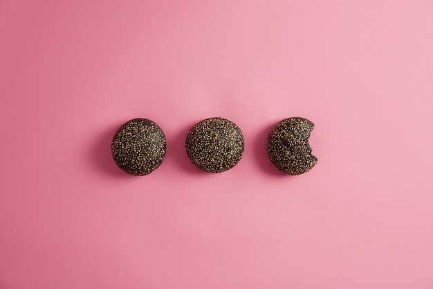 Soft round black burger buns mades of ink of cuttlefish, sprinkled with sesame, ready for making vegetarian sandwiches. One bread is bitten. Unhealthy nutrition, junk food concept. Takeaway cuisine