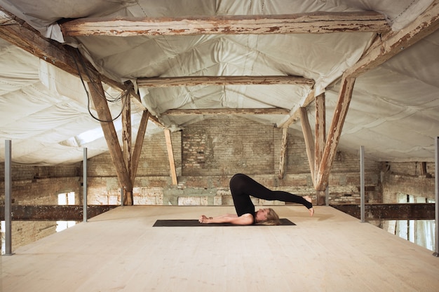 Soft. A young athletic woman exercises yoga on an abandoned construction building. Mental and physical health balance. Concept of healthy lifestyle, sport, activity, weight loss, concentration.