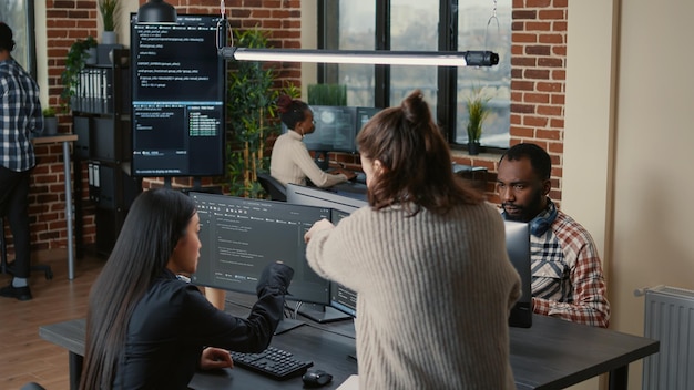 Software programer pointing pencil at source code on computer screen explaining algorithm to coworker standing next to desk. Programmers discussing online cloud computing with team.