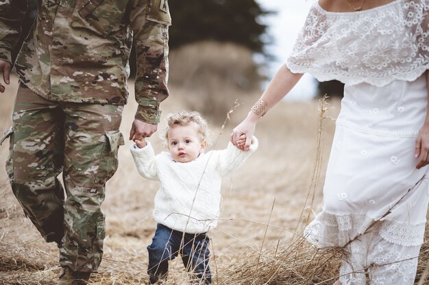 Soldier father with his wife holding the hands of their son from both sides and walking in a field