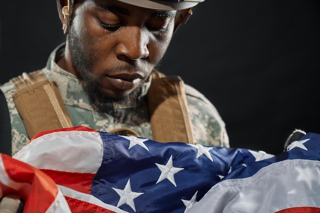Soldier in helmet sadly looking at national flag