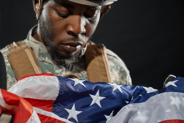 Free photo soldier in helmet sadly looking at national flag