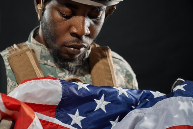 Солдат в каске грустно смотрит на национальный флаг