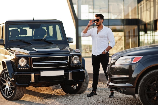 Foto gratuita solido uomo asiatico in camicia bianca e occhiali da sole posato vicino a suv mafiosi neri