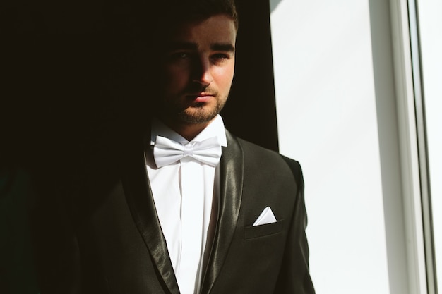 Solid brunette groom in black suit indoor sunlight