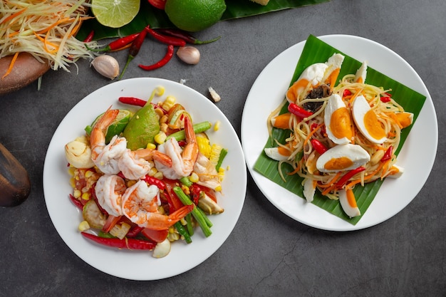 Сом Тум с кукурузой и креветками, подается с рисовой лапшой и зеленым салатом. Украшен ингредиентами тайской кухни.
