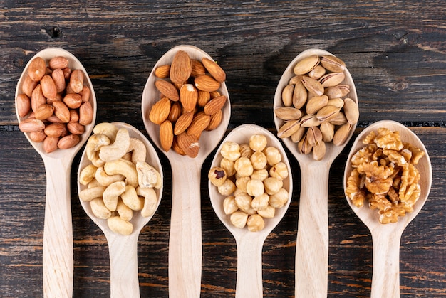 Some of assorted nuts and dried fruits with pecan, pistachios, almond, peanut, cashew, pine nuts in a wooden spoons