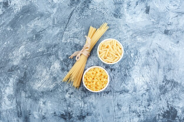 Some assorted pasta in bowls on grey plaster background, top view.