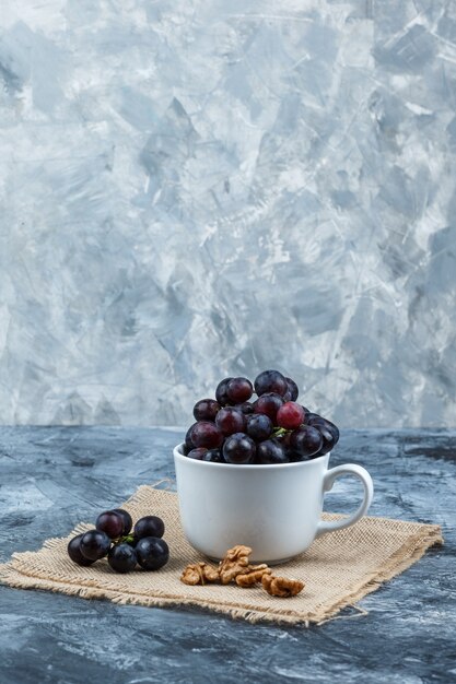 Some black grapes with walnuts in a white cup on grunge and piece of sack background, side view.