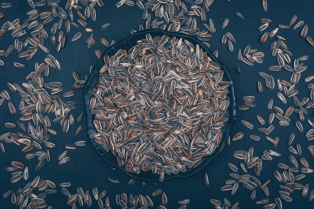 Some black sunflower seeds in a plate on black background, top view.